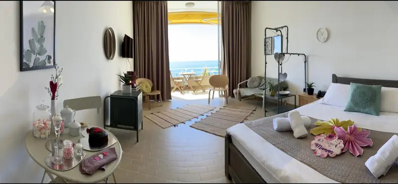 Une chambre lumineuse avec un lit et un espace salon donnant sur une vue mer.