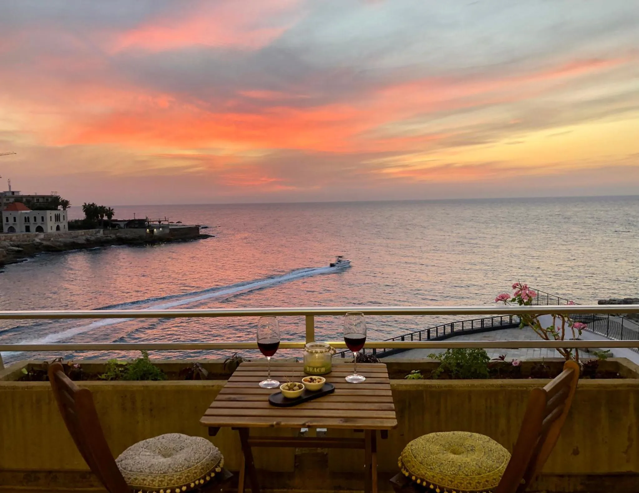 Une table avec deux verres de vin est posée sur une terrasse avec vue sur la mer au coucher du soleil.