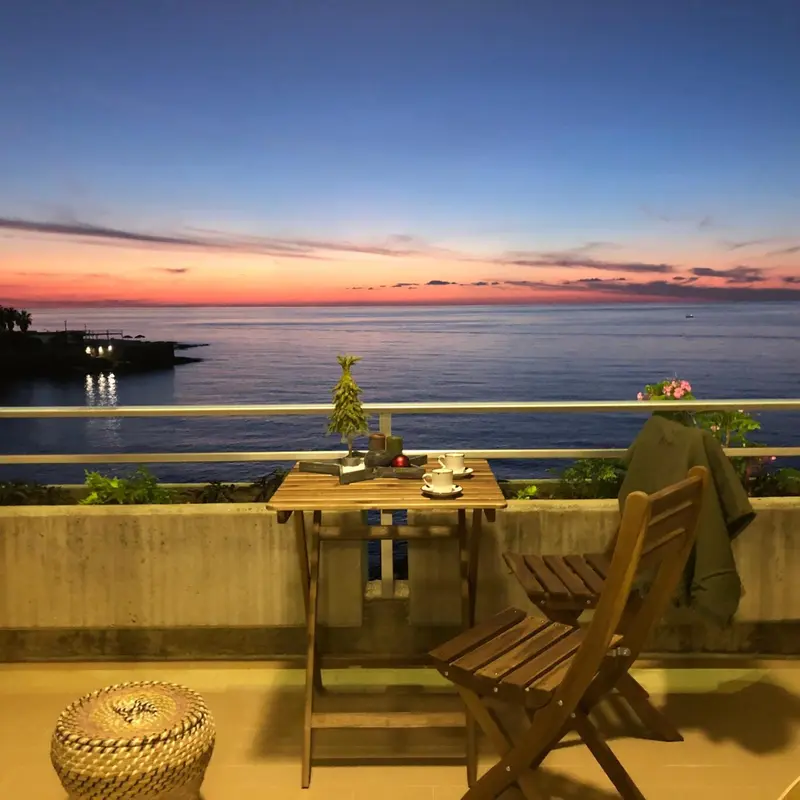 Une table et des chaises en bois sont disposées sur une terrasse avec vue sur la mer au coucher du soleil.