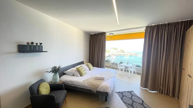 Chambre lumineuse avec un lit et un accès à une terrasse vue sur mer.