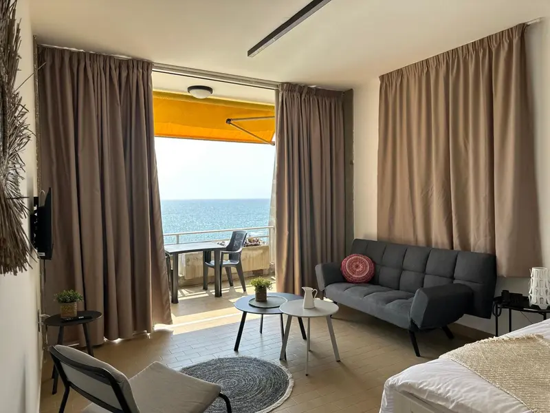 Espace de vie lumineux avec canapé et vue sur la mer depuis un balcon.