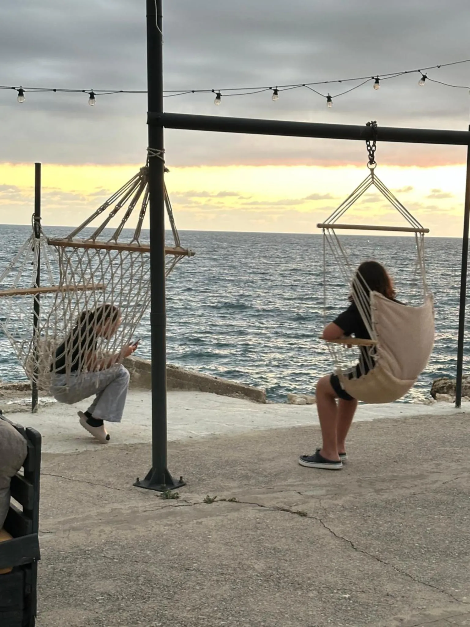 Deux personnes se détendent sur des balancelles face à la mer au coucher du soleil.