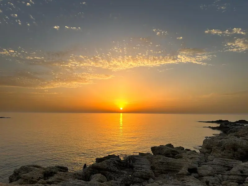 Coucher de soleil sur la mer avec des rochers au premier plan.