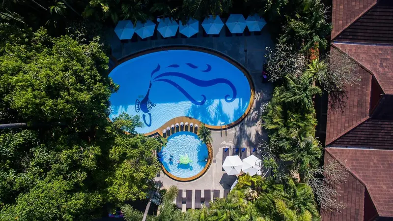 Vue aérienne d'une piscine en forme d'étoile de mer entourée de végétation luxuriante et de bâtiments aux toits rouges.