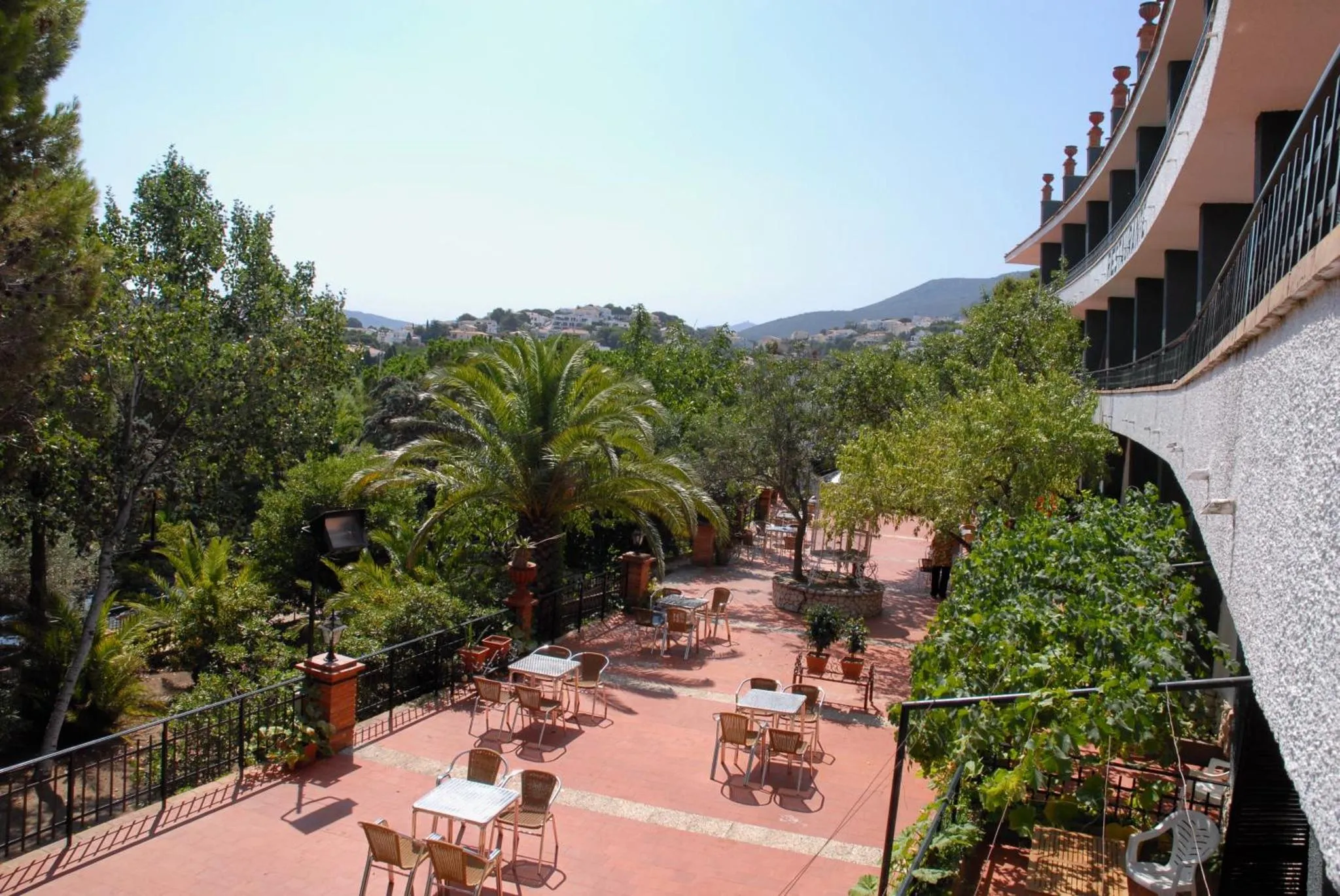 Terrasse ombragée avec tables et chaises donnant sur un paysage verdoyant.