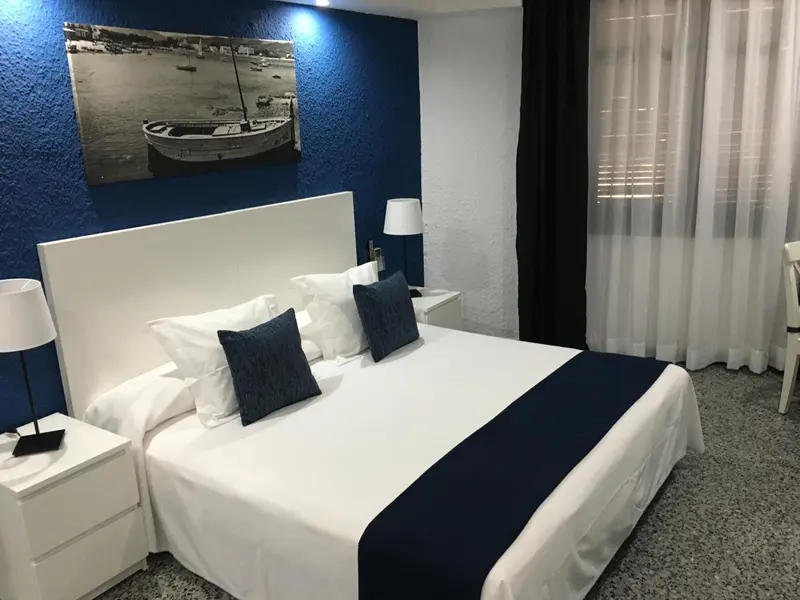 Une chambre lumineuse avec un grand lit blanc et un tableau représentant un bateau.