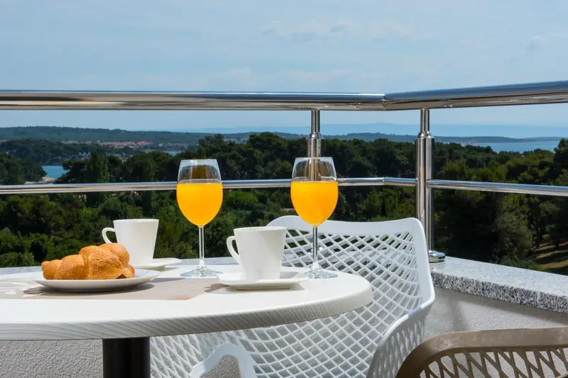 Une table avec des boissons et un croissant sur une terrasse ensoleillée.