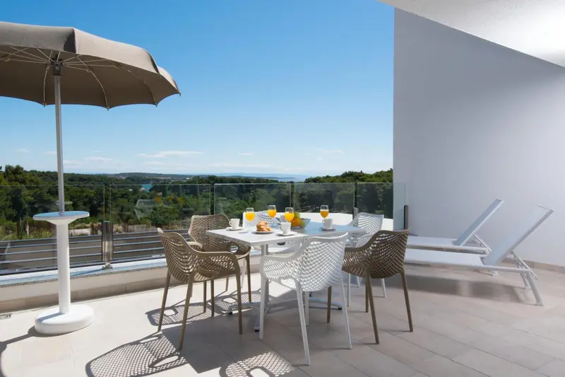 Une table avec des verres et des viennoiseries est mise en scène sur une terrasse ensoleillée.