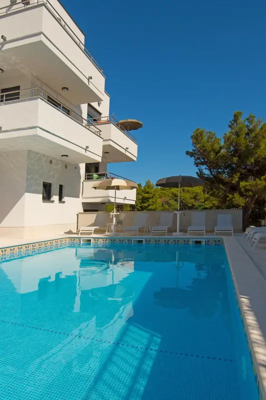 Une piscine turquoise reflète un bâtiment blanc sous un ciel bleu dégagé.