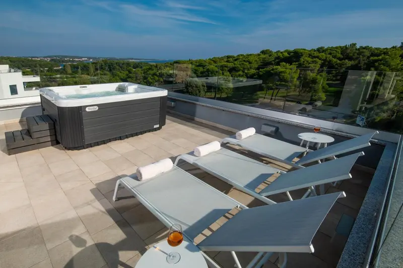 Terrasse avec jacuzzi et chaises longues offrant une vue sur la mer et la végétation.
