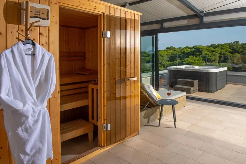Un sauna en bois ouvert sur une terrasse avec jacuzzi et mobilier de détente.