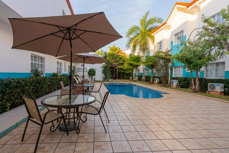 Terrasse carrelée avec mobilier de jardin près d'une piscine et d'un bâtiment blanc.
