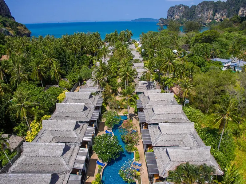 Vue aérienne d'un complexe hôtelier bordé de palmiers et traversé d'une piscine sinueuse.
