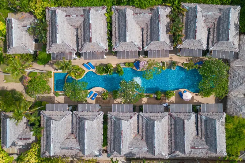 Vue aérienne d'un complexe hôtelier avec piscine sinueuse et végétation tropicale.