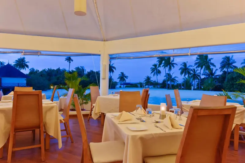 Une salle à manger lumineuse avec des tables dressées face à l'océan.