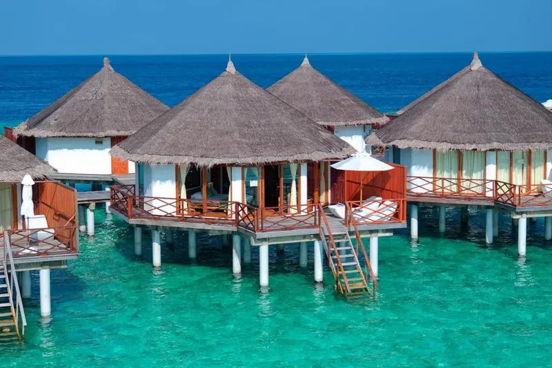 Plusieurs bungalows sur pilotis au-dessus d'une eau turquoise.