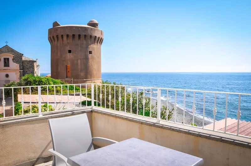 Vue d'une terrasse avec une table et une chaise donnant sur la mer et un bâtiment historique.