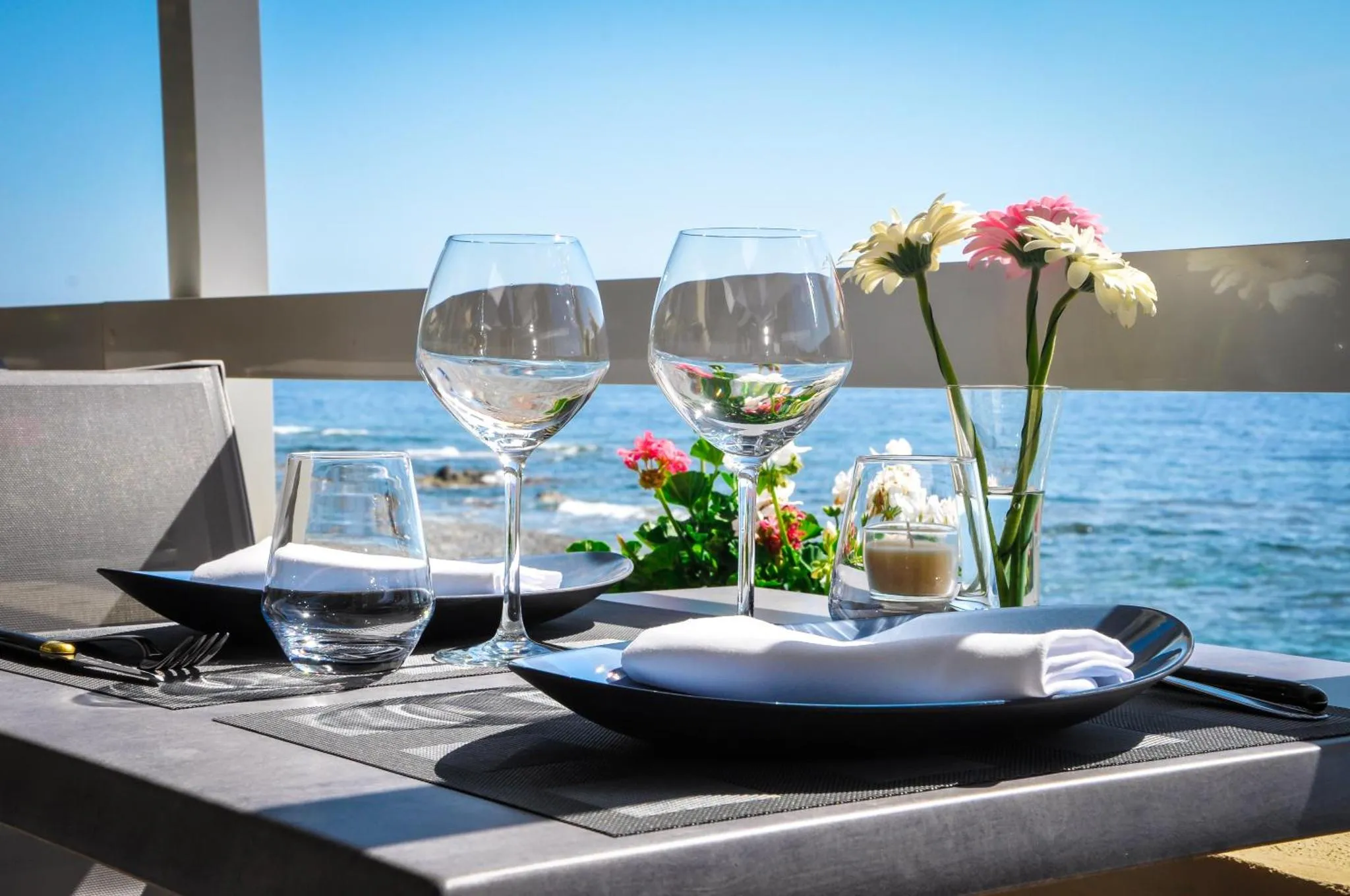 Une table dressée avec des verres et de la vaisselle, face à la mer.