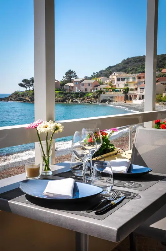 Une table dressée avec de la vaisselle et des fleurs face à la mer.