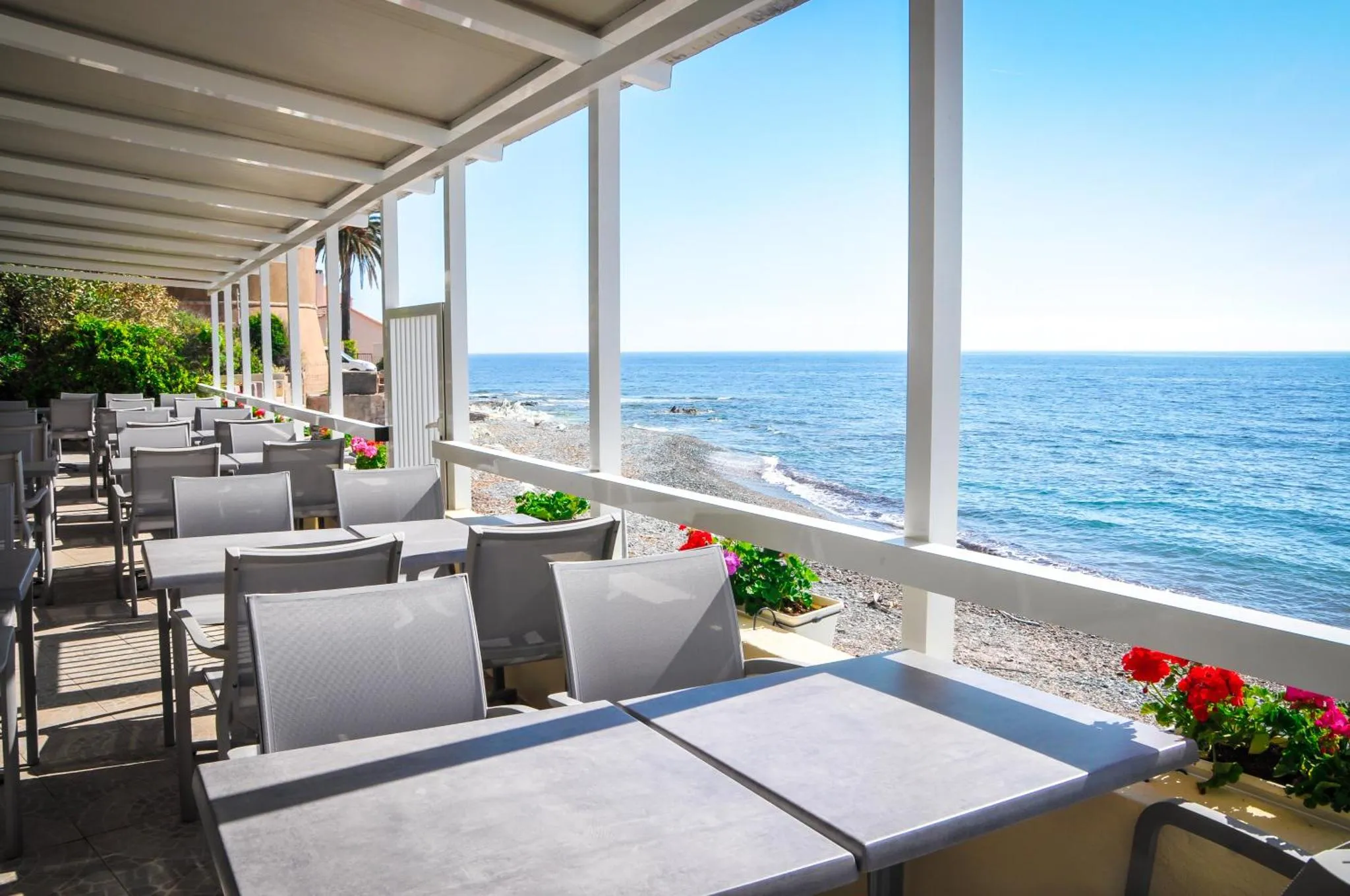 Terrasse ombragée avec tables et chaises donnant sur la mer.