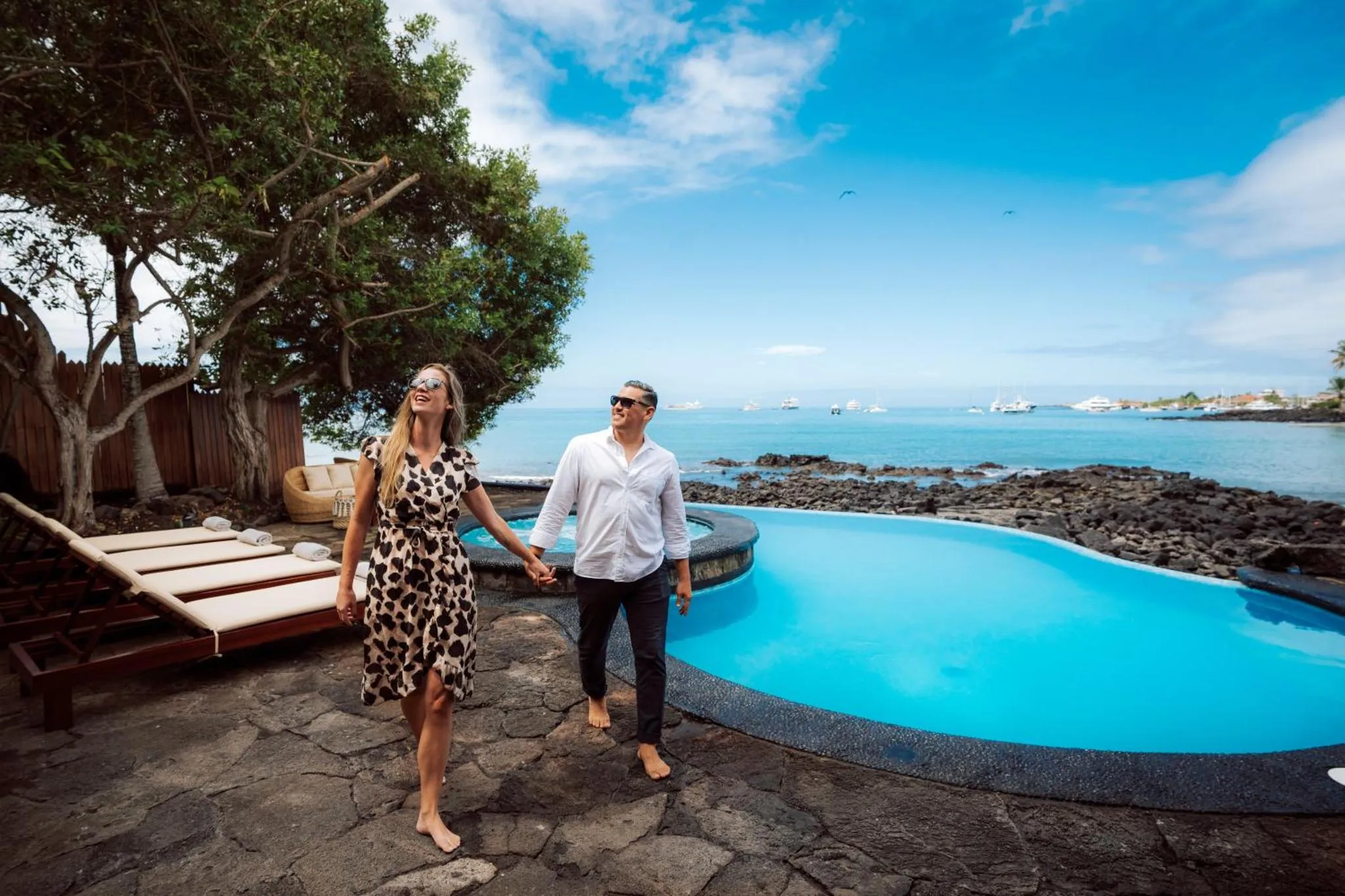 Un couple se promène près d'une piscine turquoise en bord de mer.