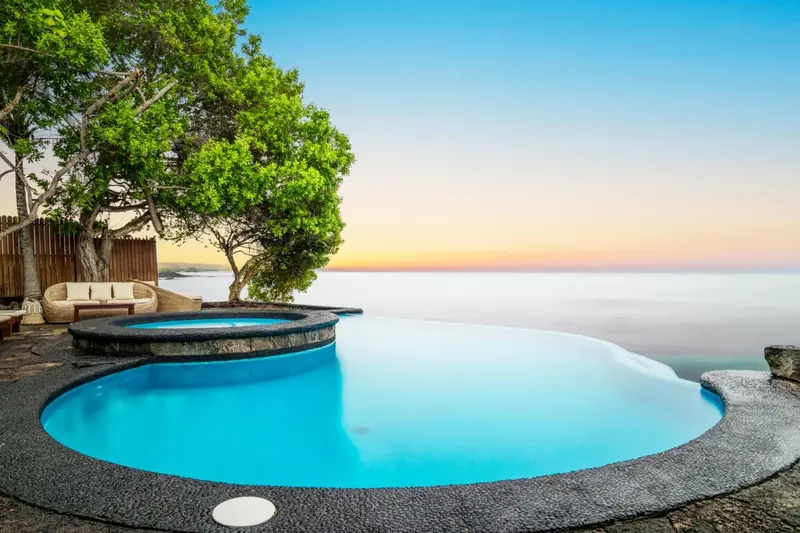 Une piscine à débordement surplombe la mer au coucher du soleil.
