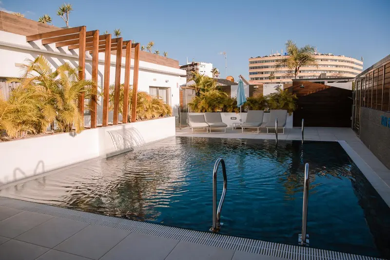 Une piscine rectangulaire avec des transats et une cascade artificielle.
