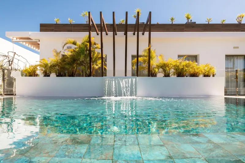 Une piscine turquoise avec une cascade artificielle et une végétation luxuriante.