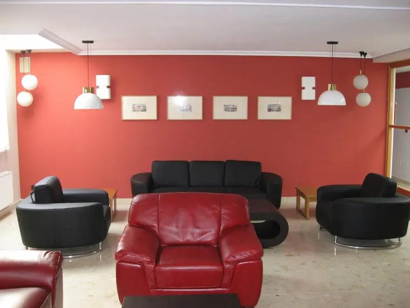 Un salon moderne avec des fauteuils en cuir et des tableaux décoratifs sur un mur rouge.