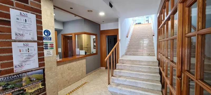Hall d'entrée lumineux avec comptoir d'accueil et escalier.