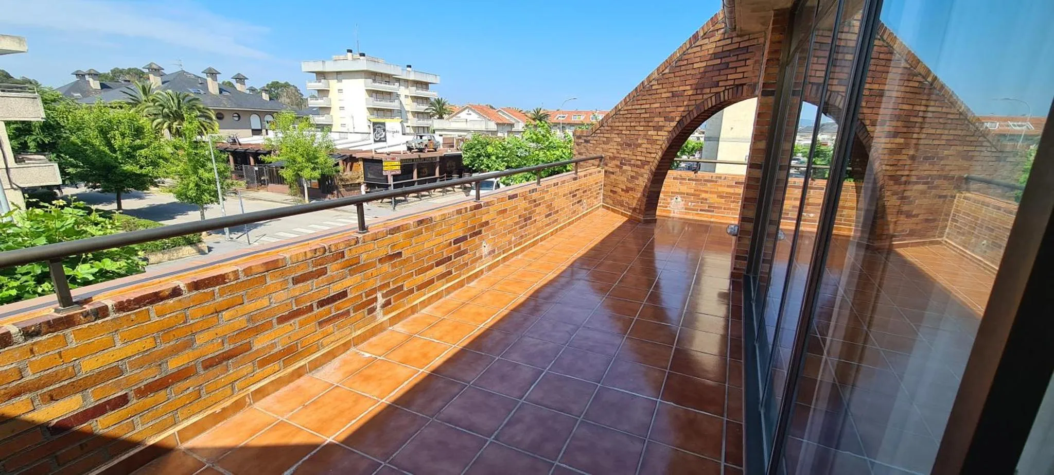 Terrasse carrelée avec garde-corps en métal et vue sur la ville.