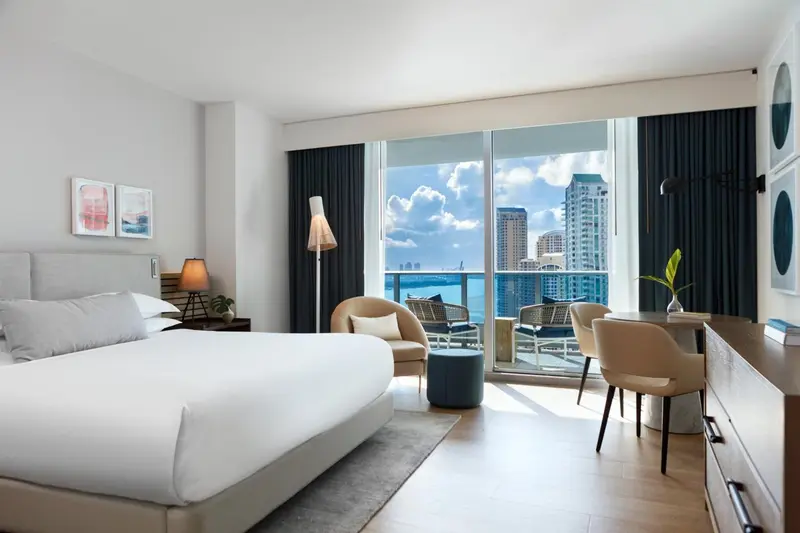 Chambre lumineuse avec un grand lit et une vue sur la mer depuis un balcon.