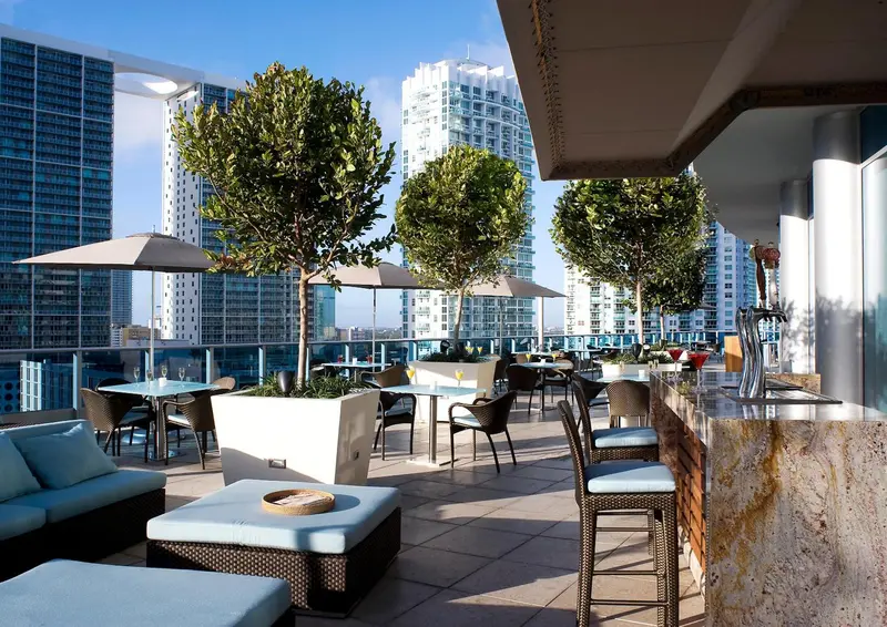 Terrasse aménagée avec tables, chaises et bar en hauteur, offrant une vue sur la ville.