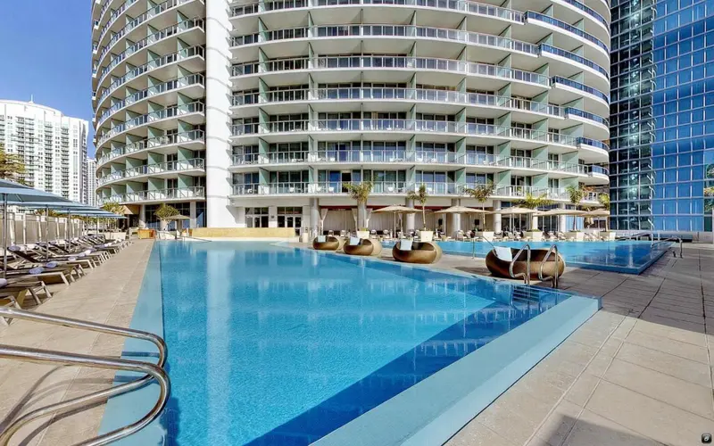 Une piscine rectangulaire avec des transats et des parasols devant un bâtiment moderne.