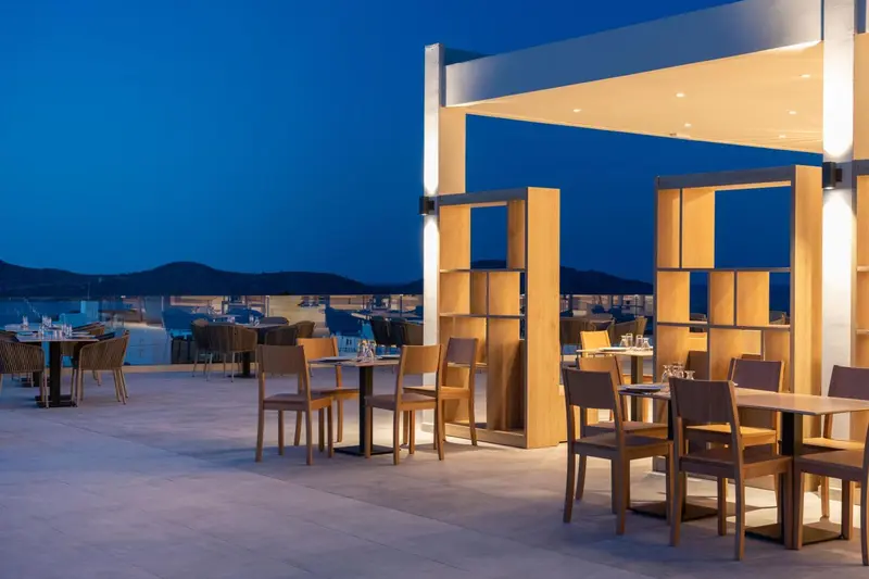 Terrasse lumineuse avec tables et chaises donnant sur une vue nocturne.