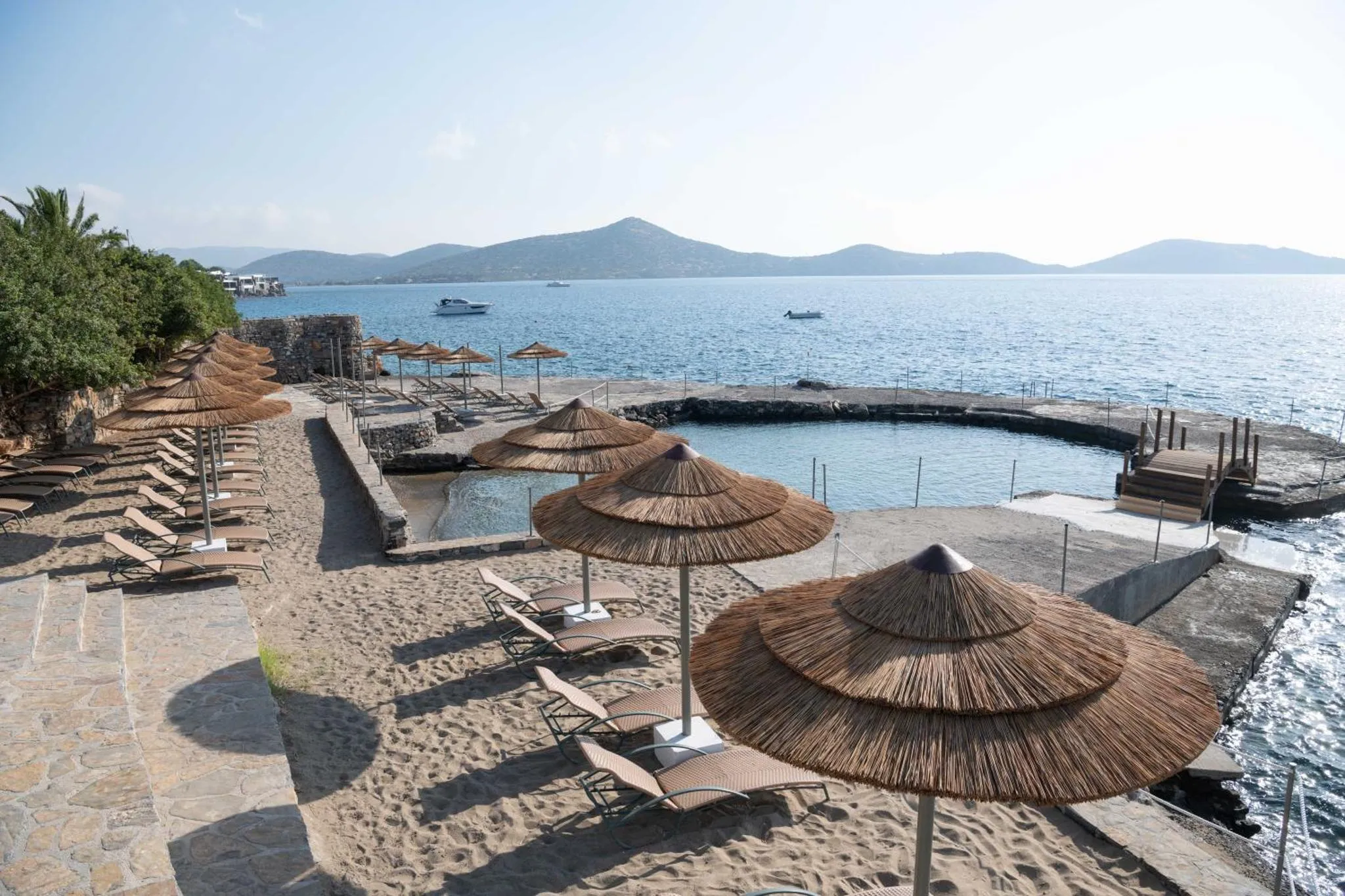 Plage de sable avec parasols de paille et transats en bord de mer.