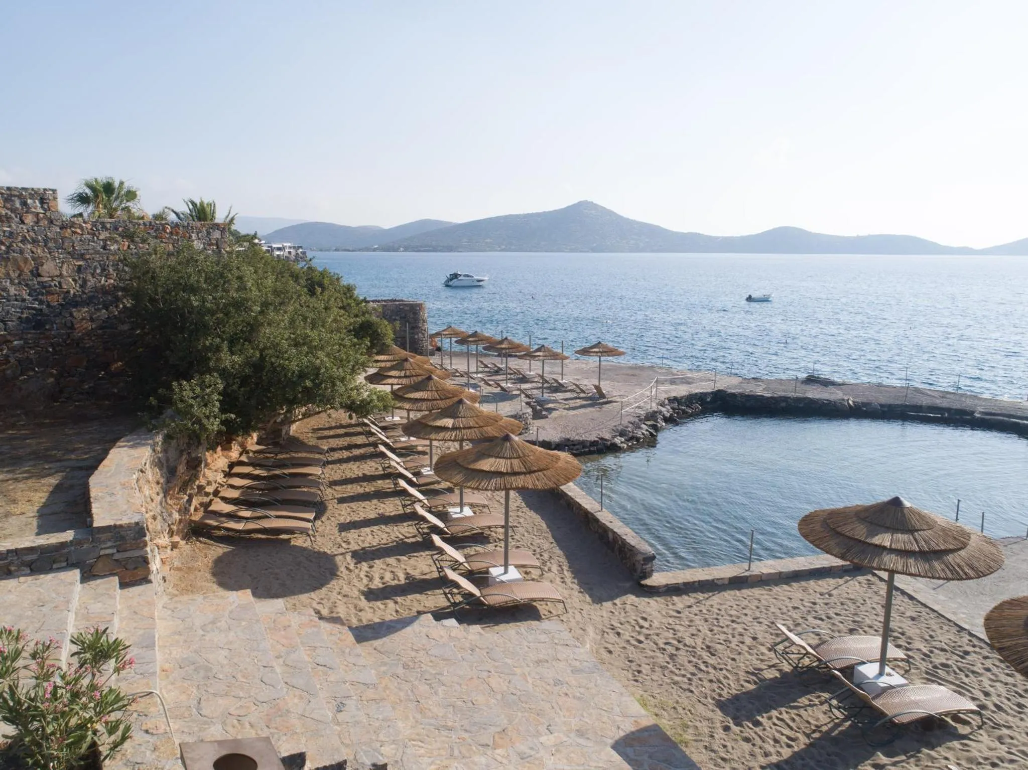 Plage de sable avec parasols et transats, vue sur la mer et les montagnes.