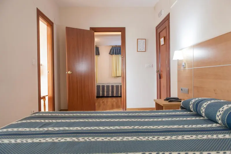 Une chambre avec un lit fait et des portes ouvertes sur d'autres pièces.