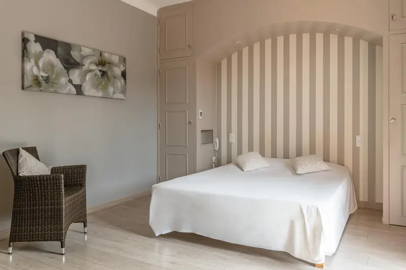 Une chambre lumineuse avec un lit recouvert d'une courtepointe blanche et un fauteuil en osier.