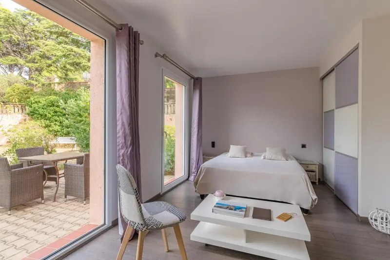Une chambre lumineuse s'ouvre sur une terrasse avec table et chaises.