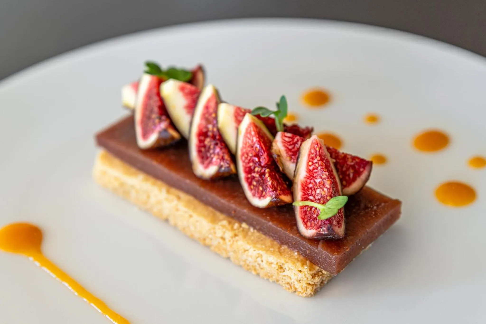 Une assiette blanche présente un dessert à base de figues fraîches et d'une crème au chocolat.