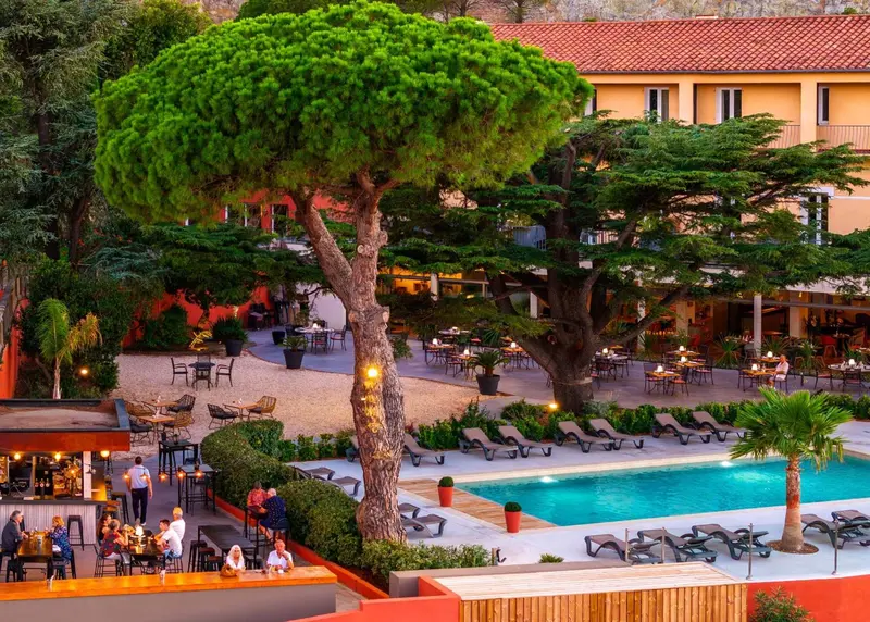 Terrasse ombragée avec tables et chaises près d'une piscine.