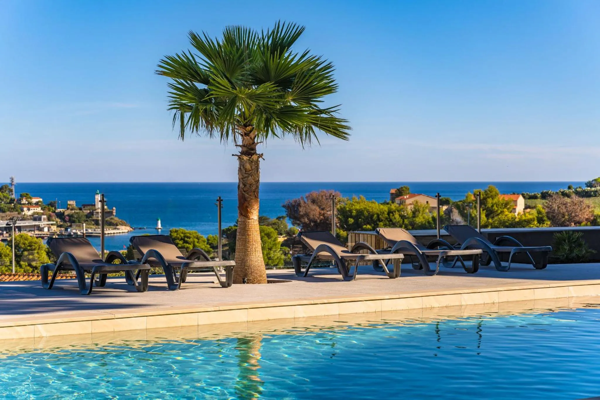 Transats alignés au bord d'une piscine avec vue sur la mer et la végétation.
