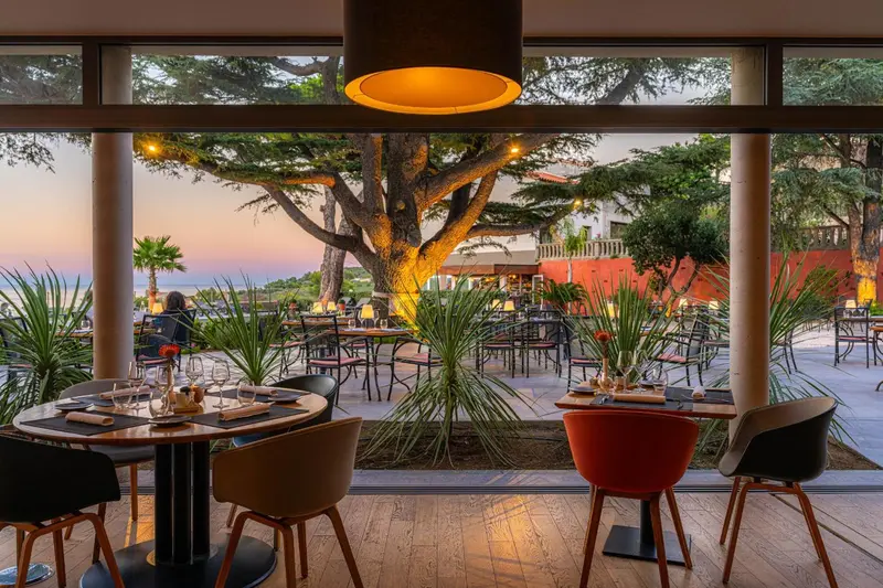 Une salle à manger lumineuse s'ouvre sur une terrasse avec vue sur la végétation et la mer.