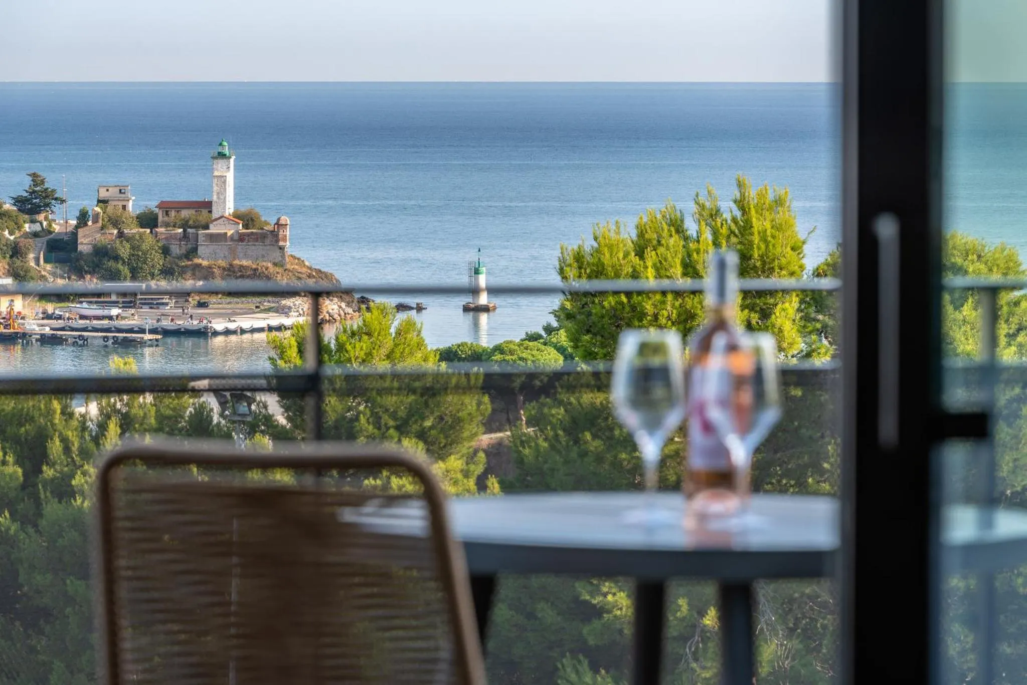 Vue sur la mer et un phare depuis une terrasse avec une table et des verres.