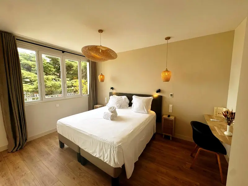Chambre lumineuse avec un grand lit et un bureau près de la fenêtre.
