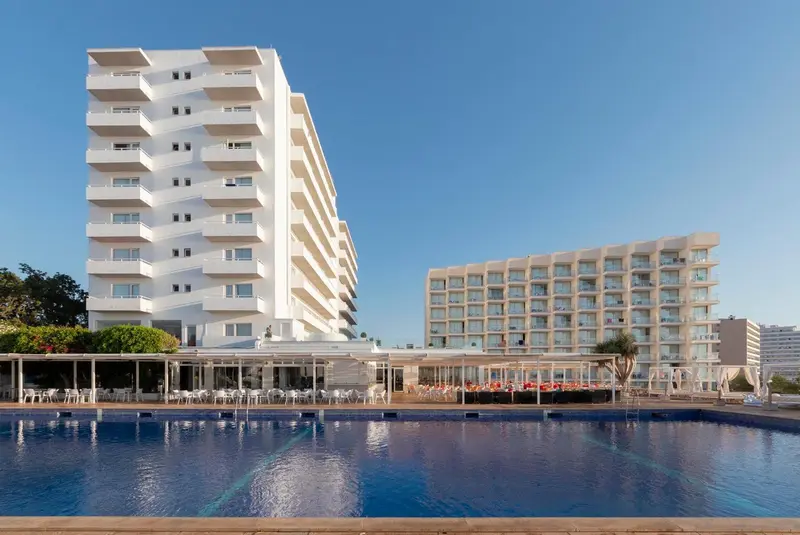 Bâtiment blanc à plusieurs étages avec des balcons surplombant une piscine bleue.