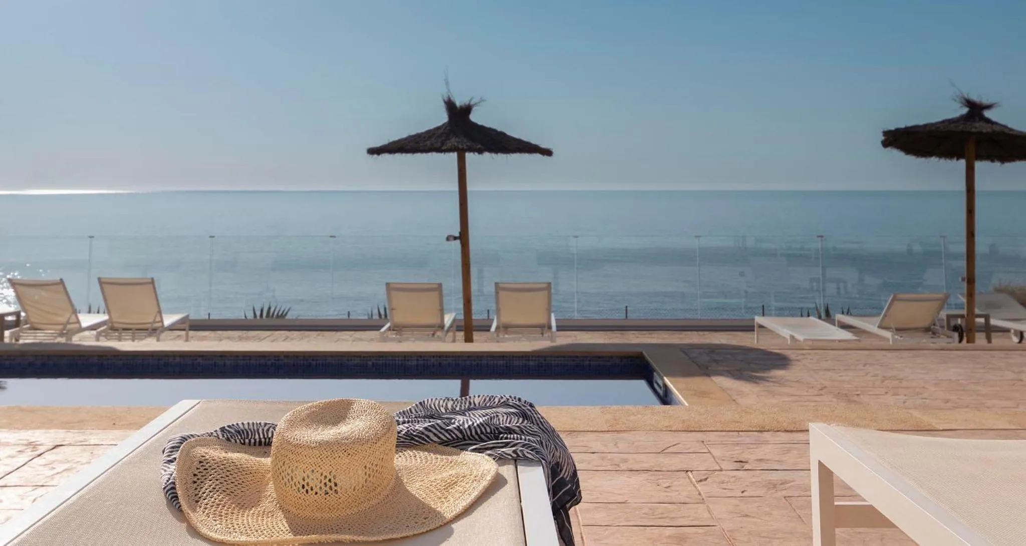 Transats et parasols bordent une piscine avec vue sur la mer.