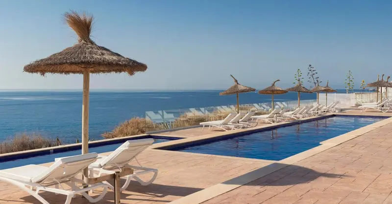 Transats blancs disposés au bord d'une piscine rectangulaire avec vue sur la mer.
