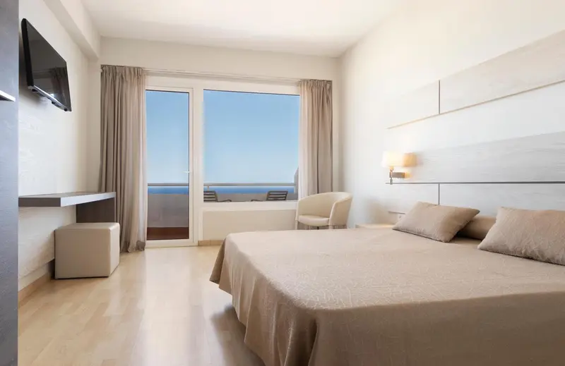 Chambre lumineuse avec un grand lit et une vue sur la mer.